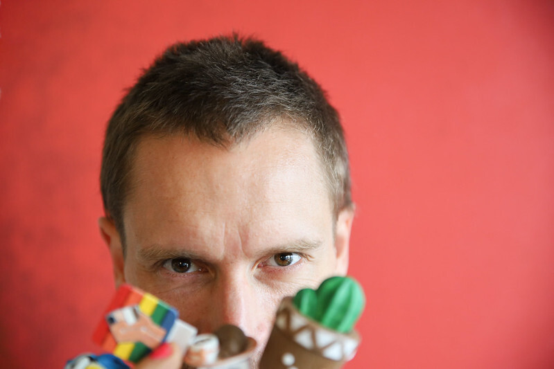 speaker portrait with red background. the speaker is holding small game figures used in his resilience rituals