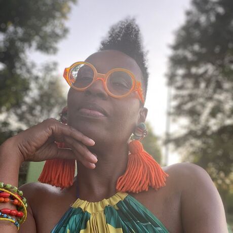 Angie in nature wearing round orange glasses in a pondering state